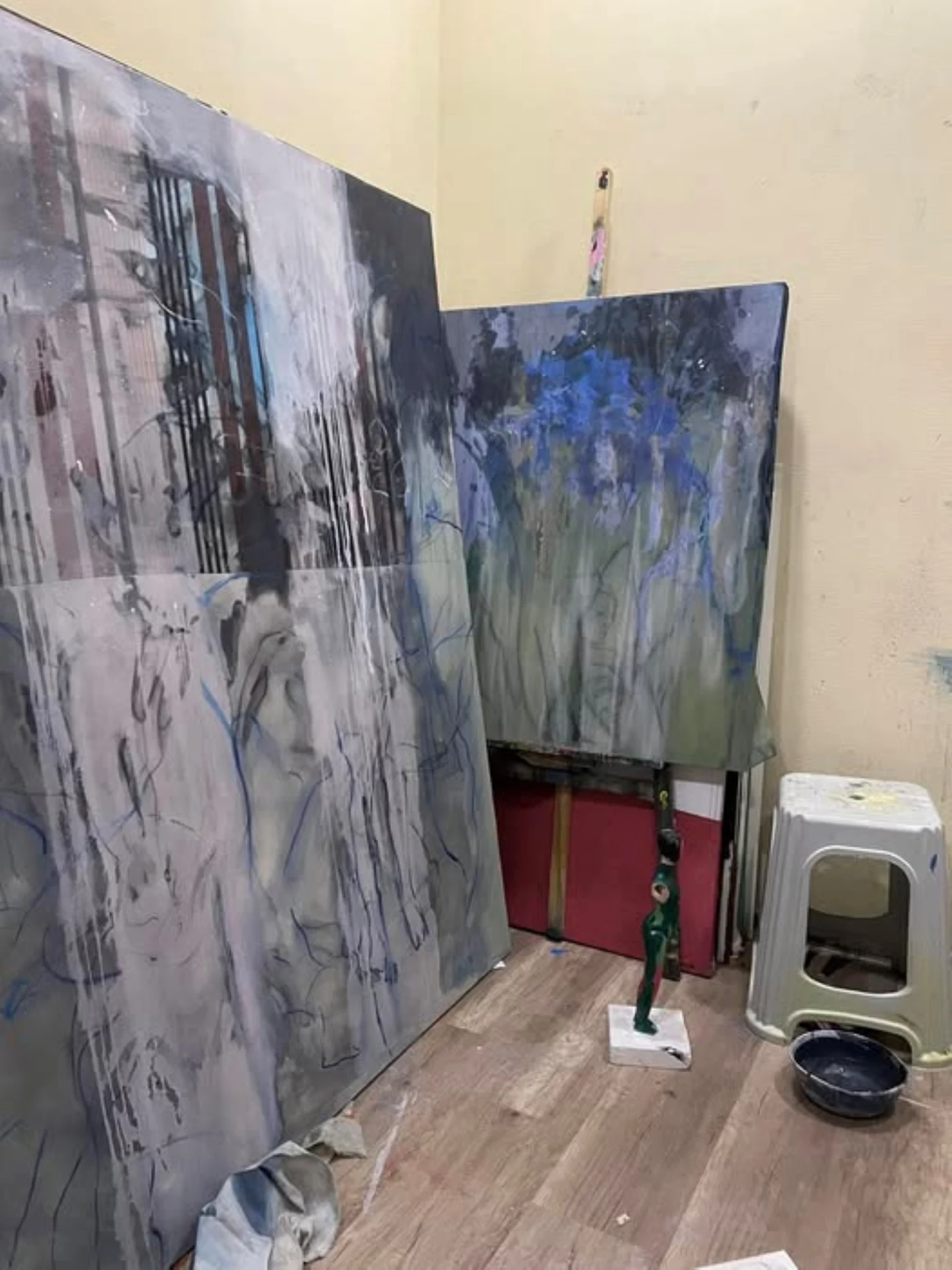 Layered paintings resting against the studio wall beside an easel